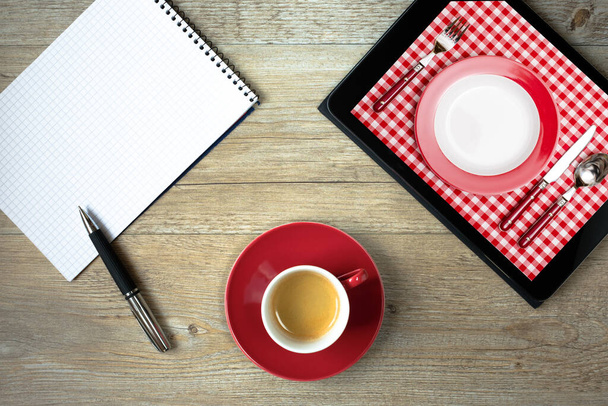 tablet with photo of dining table with place setting in red and white and block with ballpoint pen - Foto, afbeelding