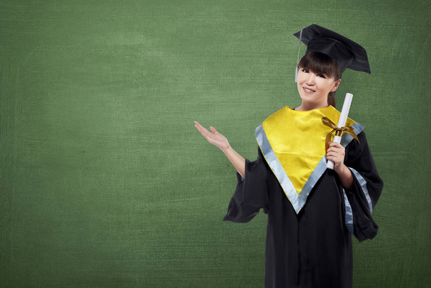 Happy asian woman with graduation cap and certificate showing copyspace on chalkboard background - Фото, зображення