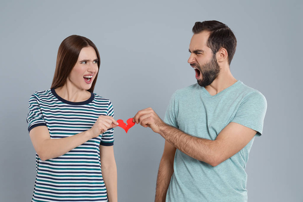 Couple tearing paper heart on light grey background. Relationship problems - Zdjęcie, obraz