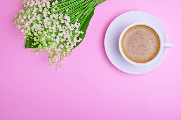 Cup of coffee and a bouquet of white lilies of the valley on a pink background, top view, empty space at the bottom - Foto, Imagem