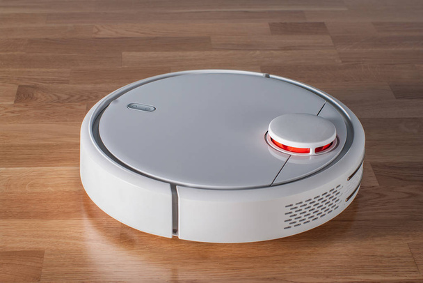 Robot vacuum cleaner runs on wood parquet floor. Modern smart cleaning technology housekeeping - Φωτογραφία, εικόνα