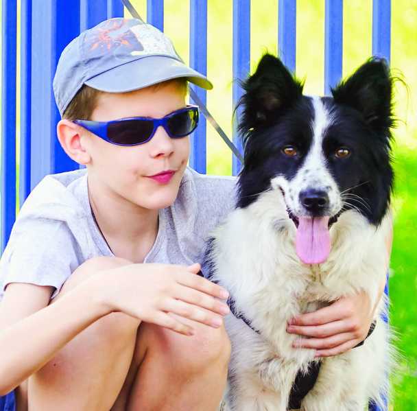 Egy fiú sötét szemüvegben ül és megölel egy kutyát.. - Fotó, kép