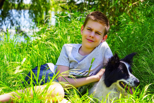 Un garçon s'assoit sur une pelouse verte et étreint un chien
. - Photo, image