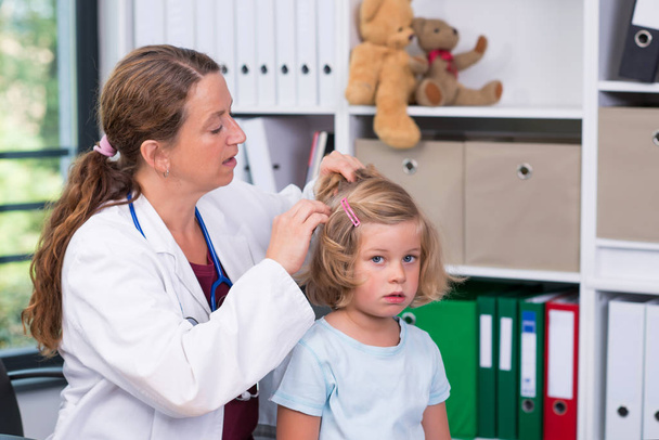 female pediatrician in white lab coat examined little girl for lice - Foto, afbeelding