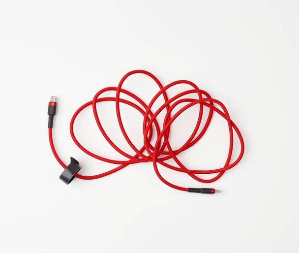 Kırmızı bir tekstil uygulamasında mobil aygıtları şarj etmek için bükülmüş kablo - Fotoğraf, Görsel