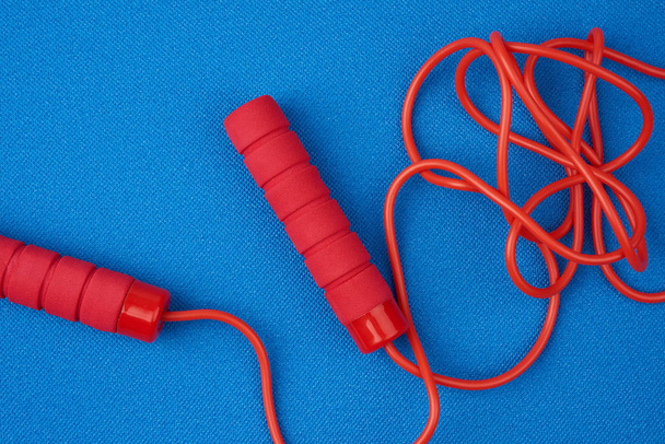 червона стрибкова мотузка лежить на неопреновому синьому спортивному килимку
 - Фото, зображення