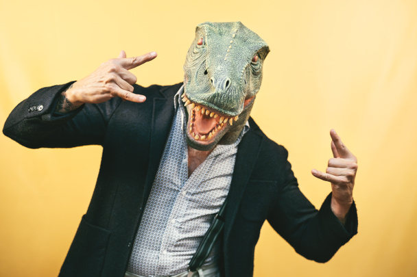 Tレックス恐竜のマスクを身に着けているシニア男-カーニバルの休日を祝う楽しみを持ってクレイジーヒップスター男-不条理とシュールな面白いコンセプト-黄色の背景 - 写真・画像