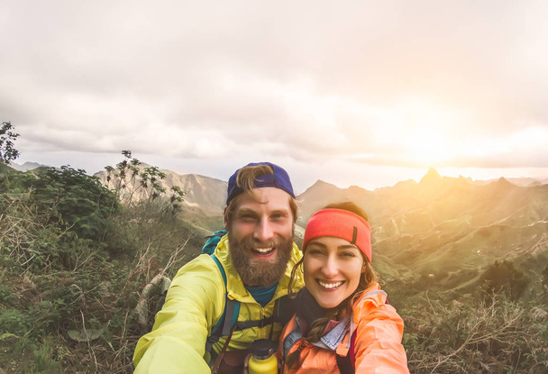 Happy couple taking selfie while doing trekking excursion on mountains - Young hikers having fun on exploration nature tour - Relationship and travel vacation lifestyle concept - Fotografie, Obrázek
