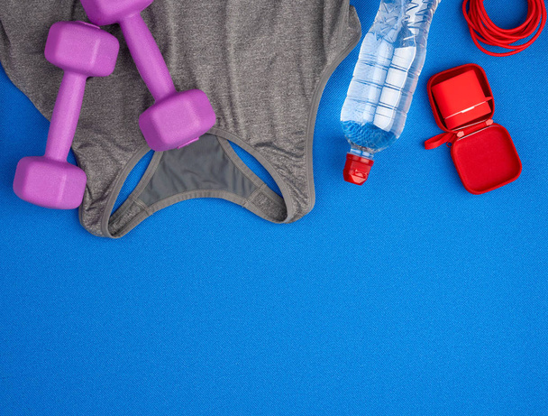 par de halteres de plástico roxo, camisa de esportes cinza em uma ba azul
 - Foto, Imagem