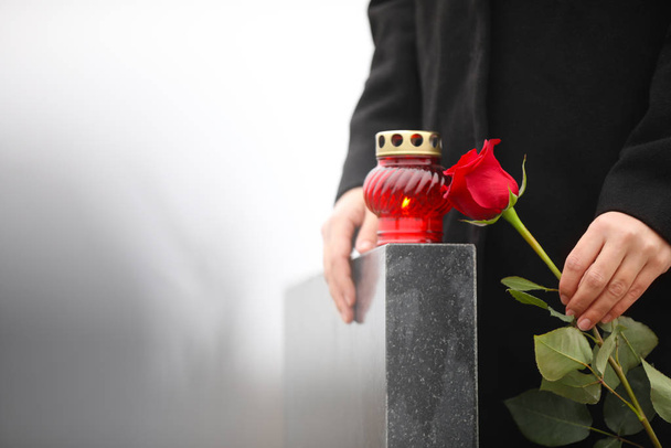 Woman holding red rose near black granite tombstone with candle  - Фото, зображення