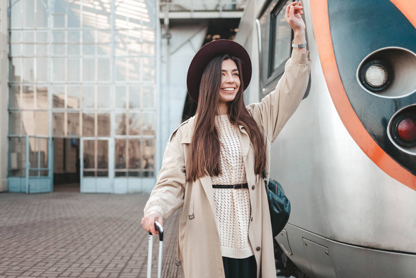 Bella viaggiatore onde la mano mentre in piedi alla stazione ferroviaria sullo sfondo di un treno
 - Foto, immagini