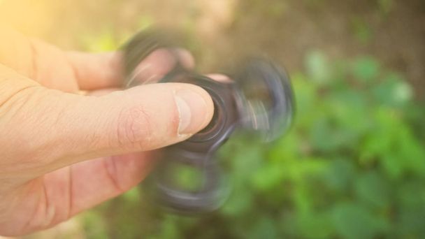 Playing with the black Fidget Spinner. Toy spinner in hand. Sun effect. - Foto, Bild