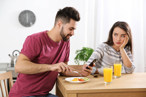 Young man preferring smartphone over his girlfriend at home - Фото, изображение