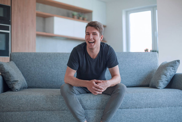young man sitting on sofa in cozy living room - Foto, afbeelding