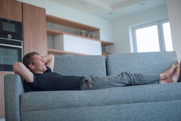 happy young man lying on sofa in cozy living room - Φωτογραφία, εικόνα