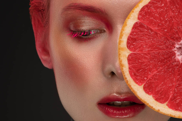 portrait of a girl with red make-up and grapefruit looking at the camera - Fotoğraf, Görsel