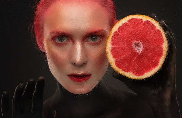 portrait of a girl with red make-up and grapefruit looking at the camera - Valokuva, kuva