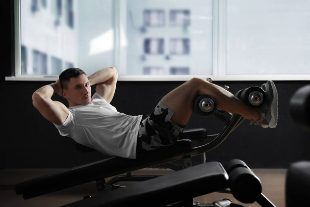 Ayarlanabilir spor yapan adam modern spor salonunda yedek kulübesinde oturur. - Fotoğraf, Görsel