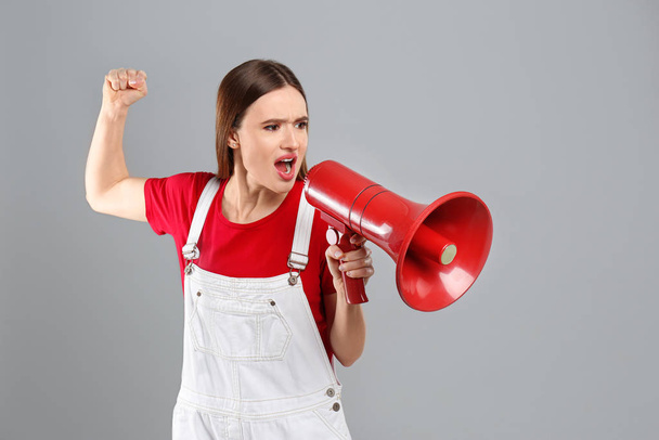 Emotional young woman with megaphone on light grey background - Photo, image