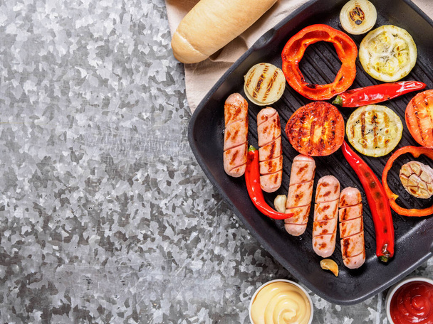Top view of chicken homemade grilled sausages in grill pan on gray metal background. Grilled sausages and grilled vegetables, buns bread, sauces ketchup and mustard. Home hot-dogs. Copy space. - Fotoğraf, Görsel