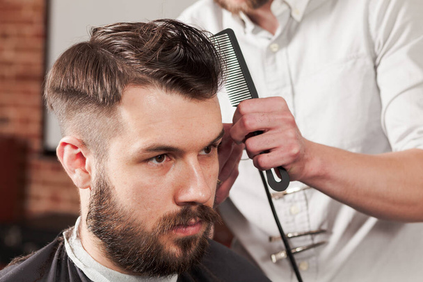 The hands of barber making haircut to attractive man in barbershop - Fotó, kép