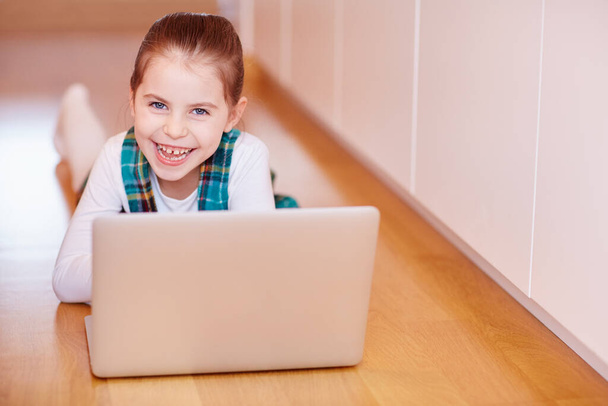 A cute little girl smiling at the camera while playing on a laptop - Фото, изображение