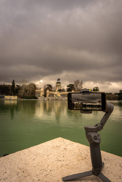 View of a smartphone doing a timelapse on an image stabilizer, in the Retiro Park in Madrid. Vertical view. Travel concept. - Photo, Image