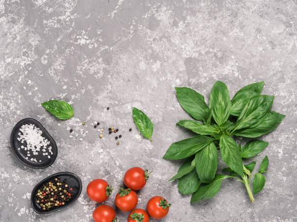 Cooking or food background. Fresh basil, tomatoes, salt and pepper on gray concrete background. Top view or flat lay Copy space. - Fotografie, Obrázek