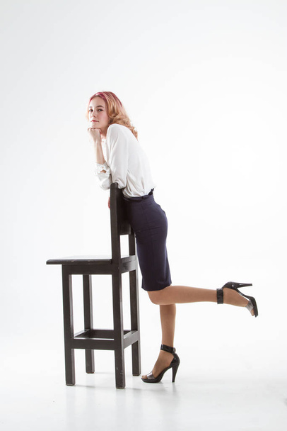 Joven mujer de negocios en una camisa blanca y falda negra está de pie junto a un taburete de la barra alta
. - Foto, Imagen