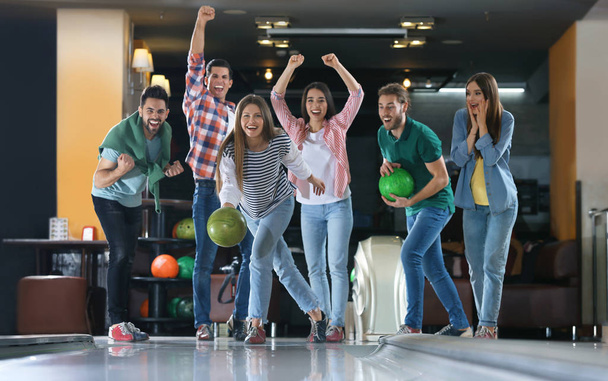 Young woman throwing ball and spending time with friends in bowling club - Photo, Image