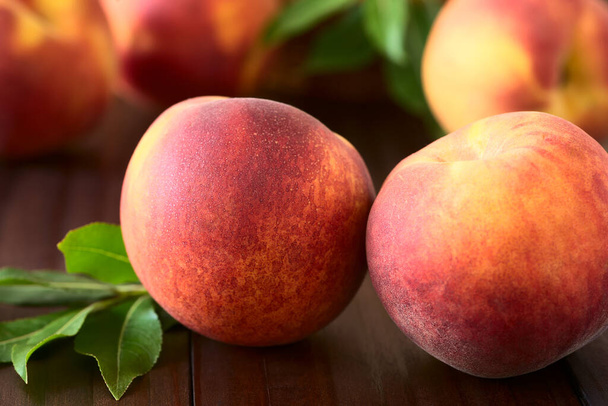 Fresh ripe peaches, photographed on dark wood with natural light (Selective Focus, Focus on the front of the front left peach) - Photo, Image