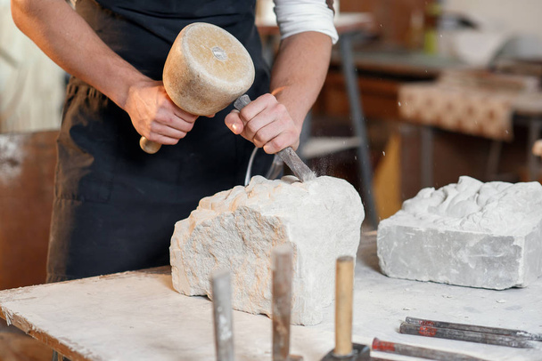 Bearded craftsman works in white stone carving with a chisel. Creative workshop with works of art. - Foto, immagini