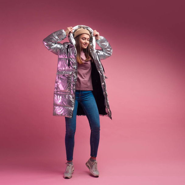fashionable and modern young woman in a puffy light down jacket throws a hood over her head. - Foto, afbeelding