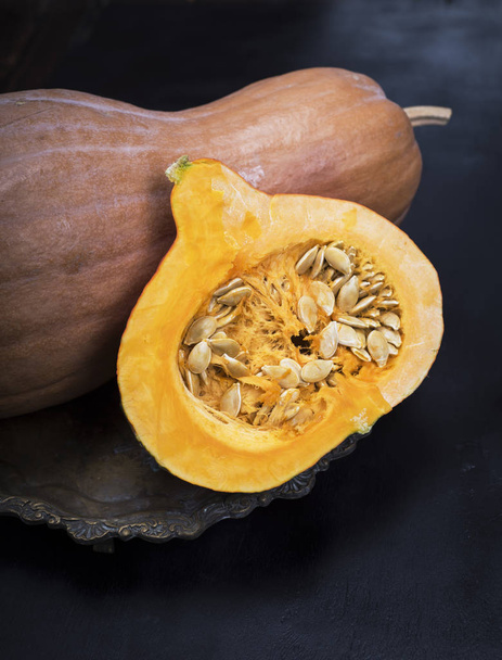 half a raw pumpkin with seeds on a copper plate, a black wooden table - Fotografie, Obrázek