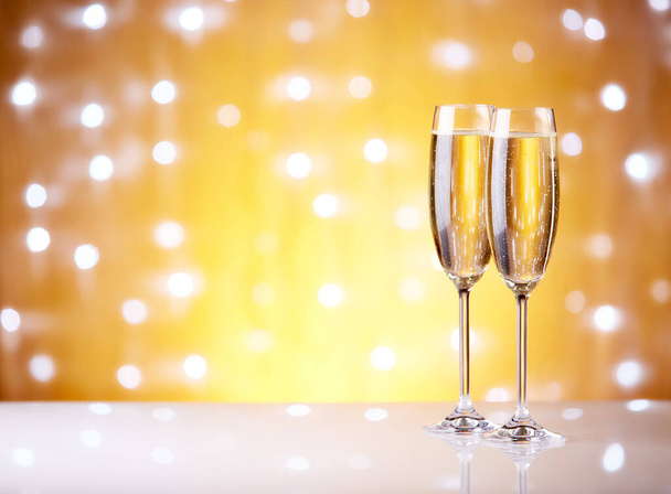 Two glasses with champange, gift boxes on a yellow background with lights of garland. - Foto, afbeelding