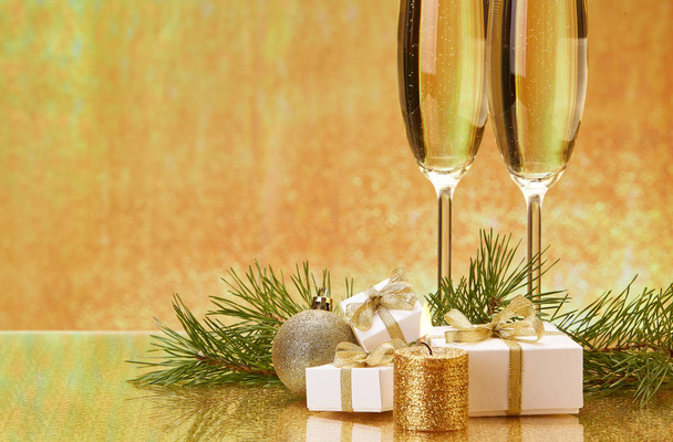 Two glasses with champange, fir tree branch, gift boxes and christmas decorations on a golden background.  New year and Christmas. - 写真・画像