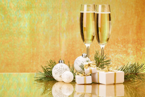 Two glasses with champange, fir tree branch, gift boxes and christmas decorations on a golden background.  New year and Christmas. - Fotografie, Obrázek