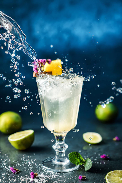 Cocktail de limonade fraîche avec citron vert, menthe et glace dans un verre à vin sur fond bleu foncé. Prise de vue studio de boisson en mouvement de gel, gouttes volantes dans éclaboussure liquide. Boisson froide et cocktail d'été
 - Photo, image