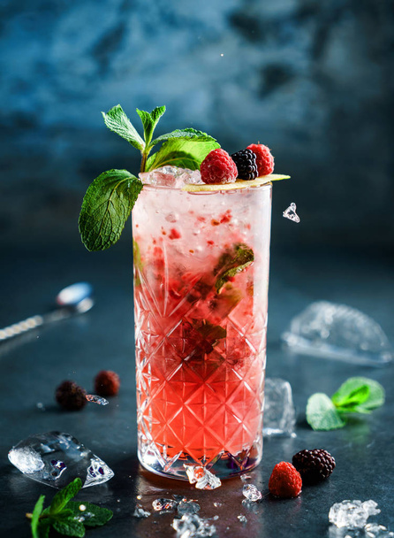 Fresh berries cocktail with raspberry, blackberry, mint and ice in jar glass on dark blue background. Studio shot of drink in freeze motion,  flying ice. Summer cold drink and cocktail - Foto, Imagem