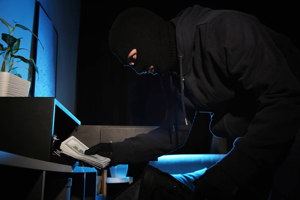 Thief taking money out of steel safe indoors at night - Foto, immagini