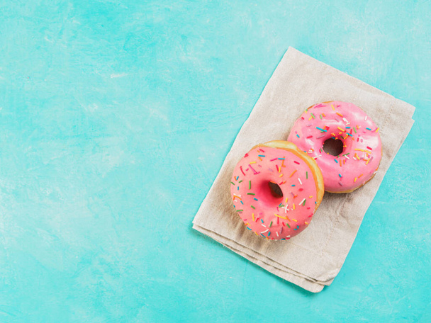 Top view of two pink donuts on blue concrete background with copy space. Colorful donuts with copyspace. Glazed doughnuts with sprinkles - Fotó, kép