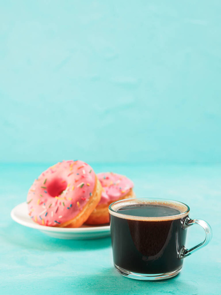 Two pink donuts and coffee on blue concrete background with copy space. Colorful donuts in plate and coffee cup with copyspace. Glazed doughnuts with sprinkles - Photo, Image
