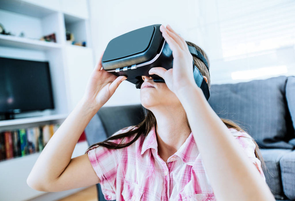 Young woman using virtual reality glasses at home, female wearing VR headset. - Photo, Image