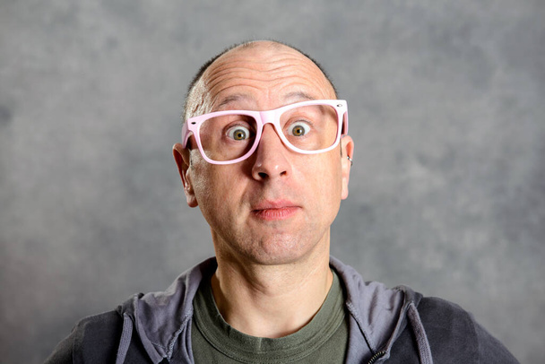 Junger Mann mit pinkfarbener Brille blickt erstaunt in die Kamera - Foto, Bild