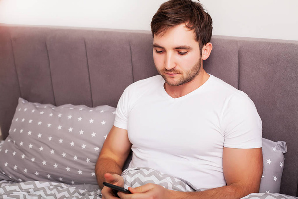 Man addicted to his mobile phone in bed - Φωτογραφία, εικόνα