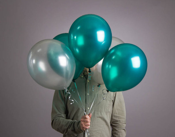 The man hides his face behind a pile of balloons. - 写真・画像