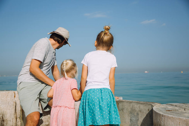 Backview of a father with two girls looking into the water - Photo, Image