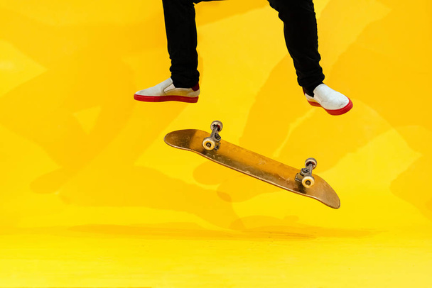Skateboarder εκτελεί skateboard τέχνασμα - κλωτσιά flip στο τσιμέντο. Ολυμπιονίκης αθλητής που προπονείται πηδάει σε κίτρινο φόντο στο στούντιο, προετοιμάζεται για το διαγωνισμό. Extreme sport, πολιτισμός της νεολαίας - Φωτογραφία, εικόνα