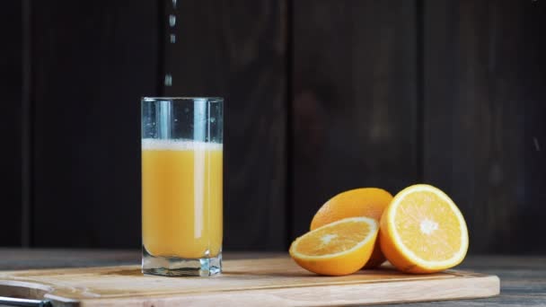 frisch gepresster Orangensaft in einem Glas auf einem hölzernen Hintergrund auspressen  - Filmmaterial, Video