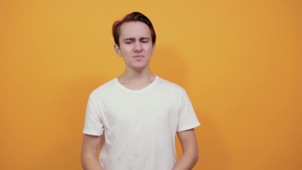 Buikpijn maagproblemen wit T-shirt jonge man op gele achtergrond. - Video